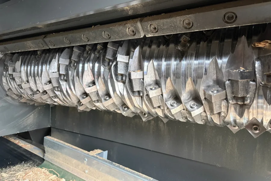 Rotor van een single shaft shredder met messen en punten, met houtsnippers eronder
